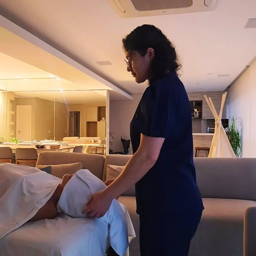 Leide atendendo uma cliente na maca, montada na sala de casa